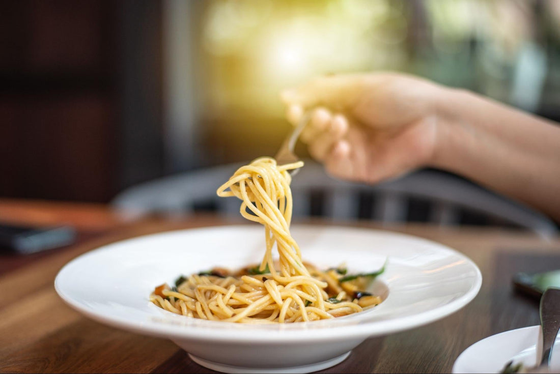A person holds a fork above a bowl of spaghetti, ready to take a bite of the delicious meal.